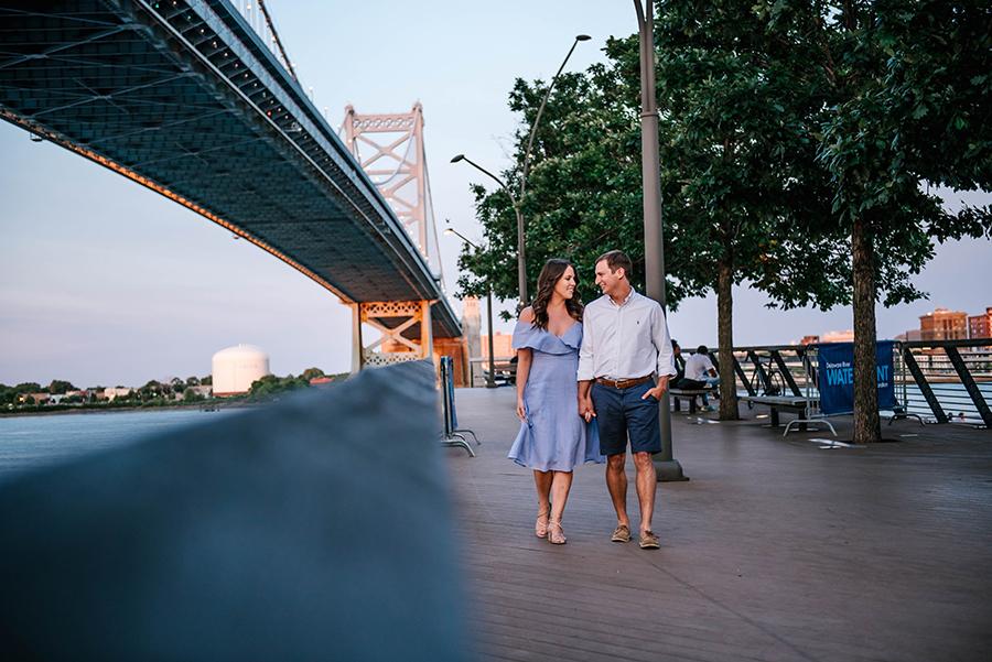 couple walk and hold hands near Ben Franklin Bridge by Nicole Cordisco and Philly In Love