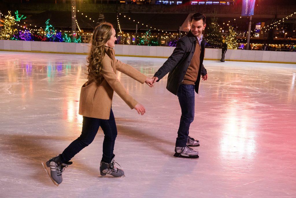 engaged couple hold hands while ice skating
