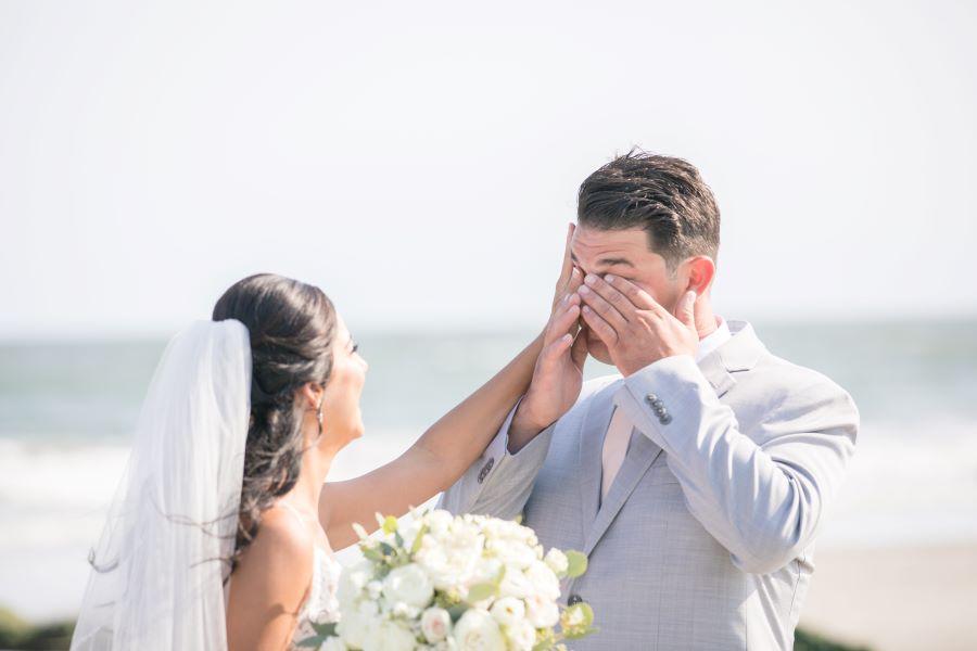 bride wipes away groom's tears on beach