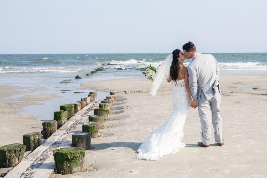 bridal couple kiss on beach by ocean